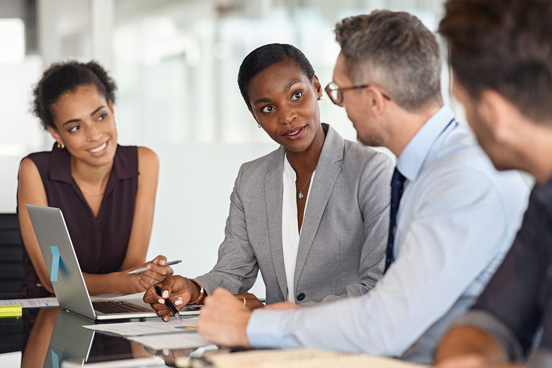 Successful business people working and discussing charts and graphs with laptop in conference room. Mature african businesswoman sharing progress on project to leader in modern office. Multiethnic business team checking new startegy on project.